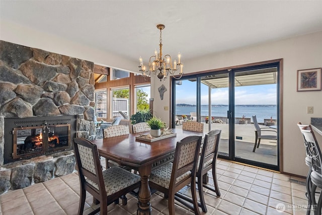 dining room with a water view, an inviting chandelier, a stone fireplace, and light tile patterned floors