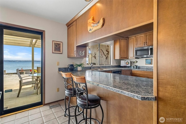 kitchen with light tile patterned flooring, dark countertops, a sink, a kitchen breakfast bar, and stainless steel microwave