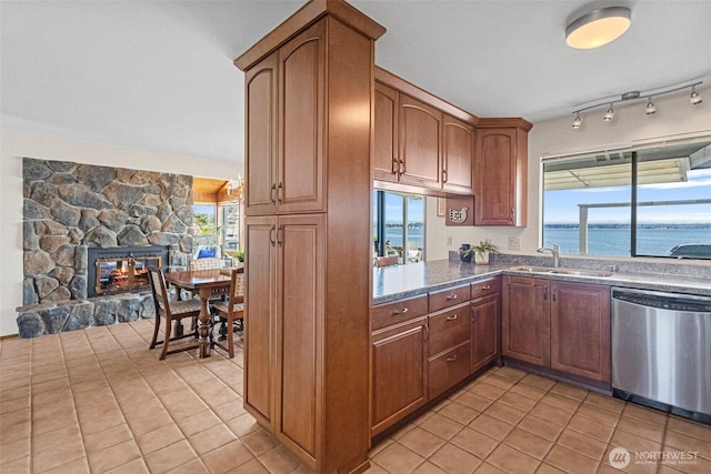 kitchen featuring a stone fireplace, dishwasher, a sink, light tile patterned floors, and open floor plan