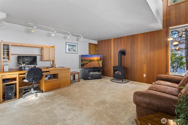 carpeted office space with track lighting, a wood stove, wood walls, and visible vents