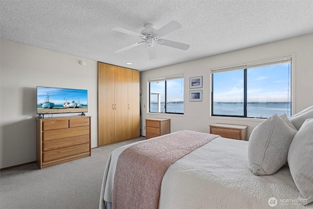 bedroom featuring a water view, a ceiling fan, a textured ceiling, and light colored carpet