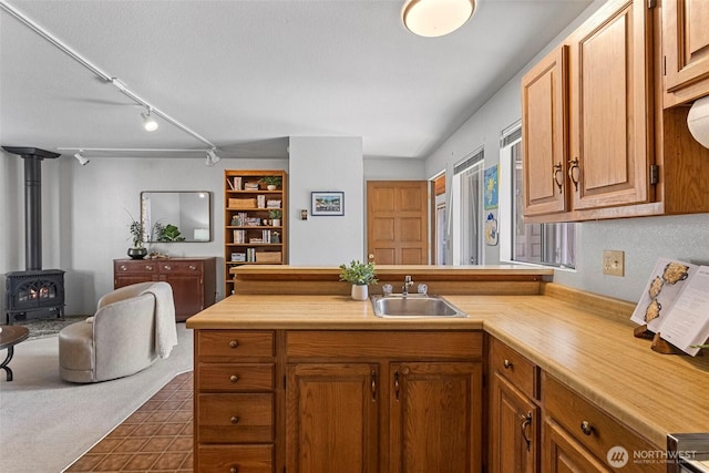 kitchen featuring a sink, a wood stove, light countertops, a peninsula, and open floor plan
