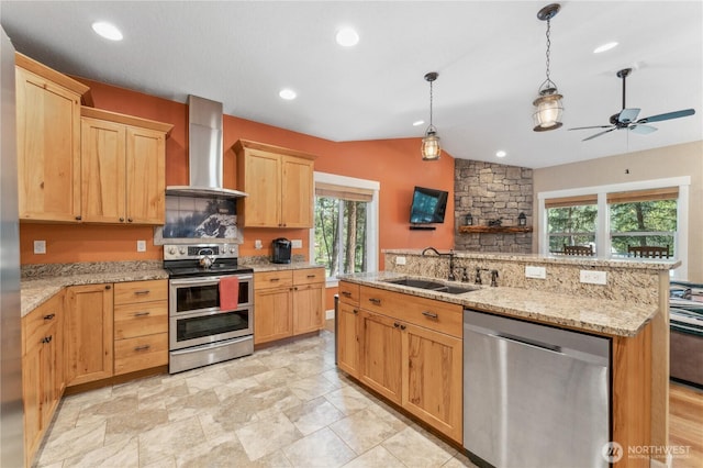kitchen featuring wall chimney range hood, light brown cabinetry, a sink, stainless steel appliances, and a ceiling fan