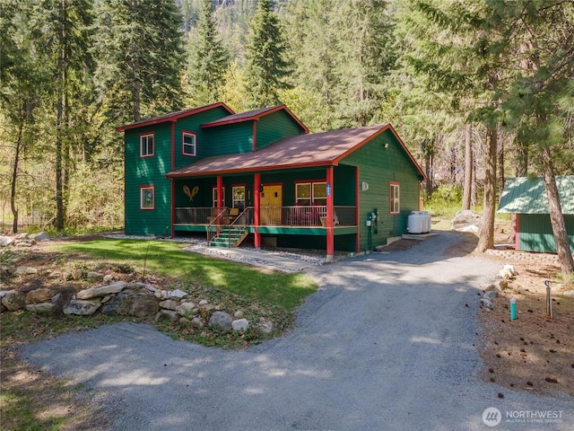 rustic home with a porch, driveway, and a wooded view