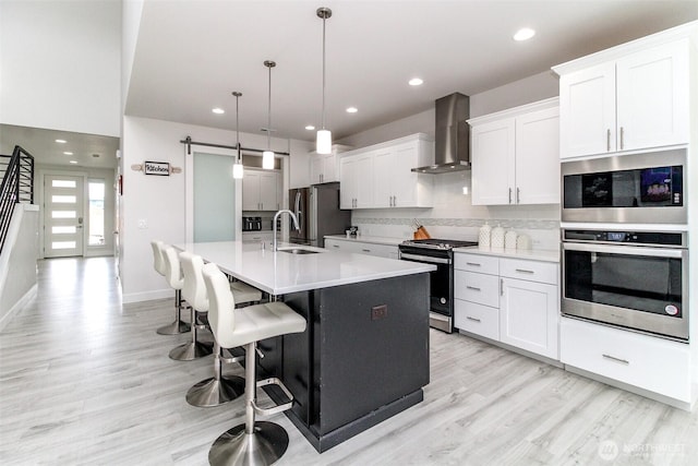 6318 230th Avenue Ct E, Buckley, WA 98321 - kitchen featuring tasteful backsplash, a kitchen island with sink, stainless steel appliances, light wood finished floors, and wall chimney exhaust hood