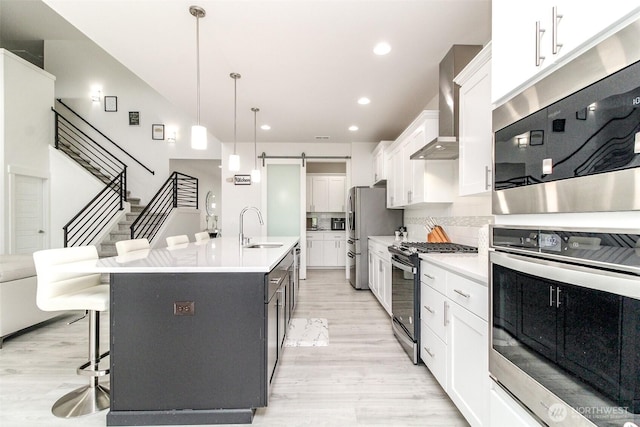 6318 230th Avenue Ct E, Buckley, WA 98321 - kitchen featuring light wood finished floors, stainless steel appliances, a kitchen breakfast bar, a sink, and wall chimney range hood