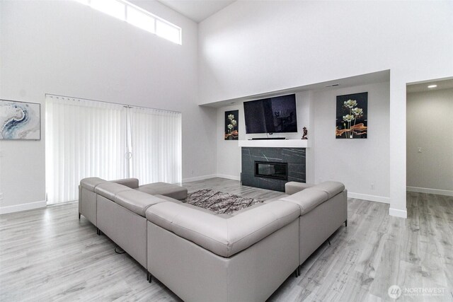 6318 230th Avenue Ct E, Buckley, WA 98321 - living room featuring a glass covered fireplace, light wood-type flooring, a towering ceiling, and baseboards