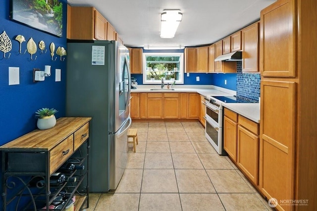 kitchen featuring stainless steel fridge, light countertops, under cabinet range hood, a sink, and double oven range