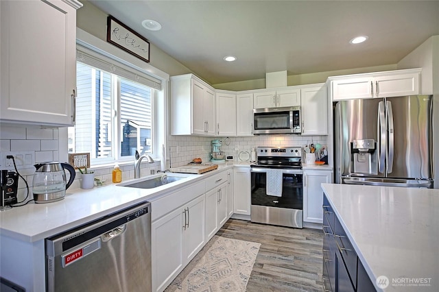kitchen with white cabinets, a sink, light wood-style floors, stainless steel appliances, and light countertops