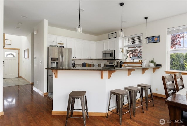 kitchen with dark stone countertops, stainless steel appliances, white cabinetry, a kitchen bar, and dark wood-type flooring