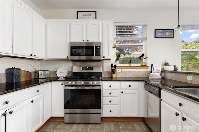 kitchen featuring dark stone counters, appliances with stainless steel finishes, white cabinets, and decorative light fixtures