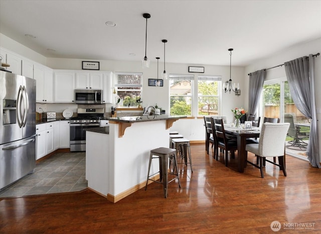 kitchen featuring dark countertops, white cabinets, a notable chandelier, a breakfast bar, and stainless steel appliances