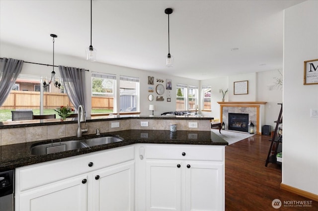 kitchen featuring hanging light fixtures, a sink, open floor plan, a high end fireplace, and dark wood-style floors