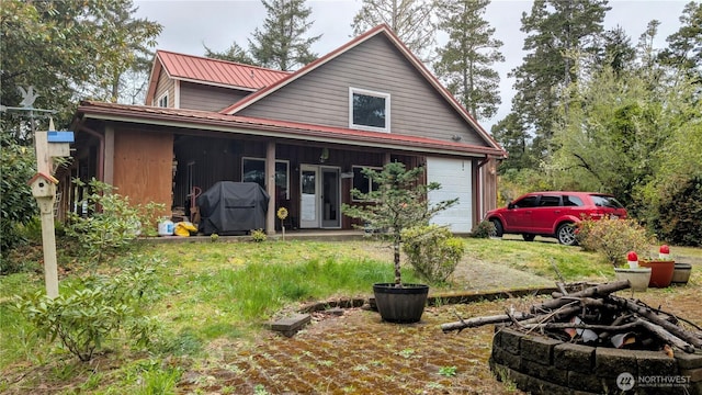 view of front of home with a garage, driveway, metal roof, and an outdoor fire pit