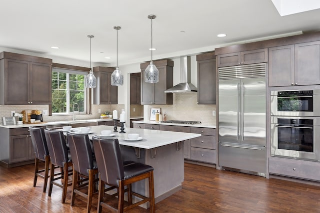 14835 NE 11th Pl, Bellevue, WA 98007 - kitchen featuring stainless steel appliances, wall chimney range hood, a sink, dark wood-style flooring, and a kitchen breakfast bar