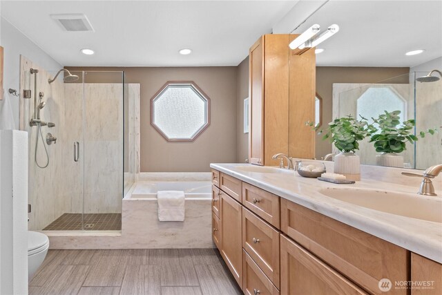 bathroom featuring a stall shower, a bath, double vanity, toilet, and recessed lighting