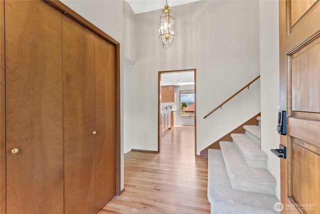 entryway with light wood finished floors, stairs, a chandelier, a high ceiling, and baseboards