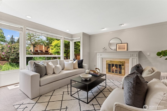 living area featuring healthy amount of natural light, ornamental molding, light carpet, and a tile fireplace
