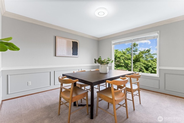 dining space with ornamental molding, light carpet, a decorative wall, and a wainscoted wall