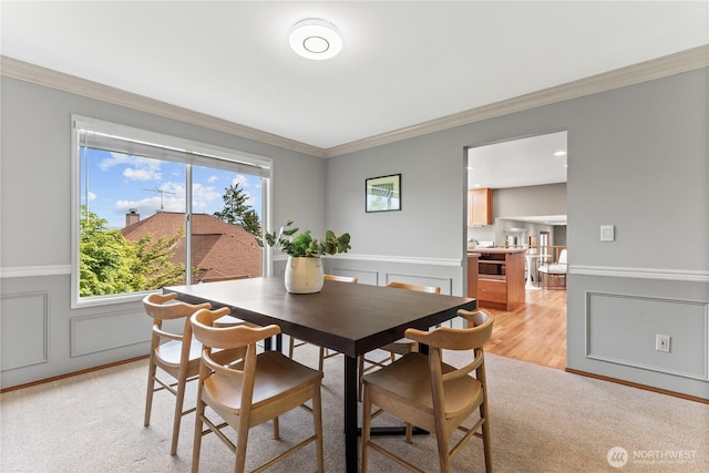 dining room with crown molding, a decorative wall, light wood-style flooring, and wainscoting