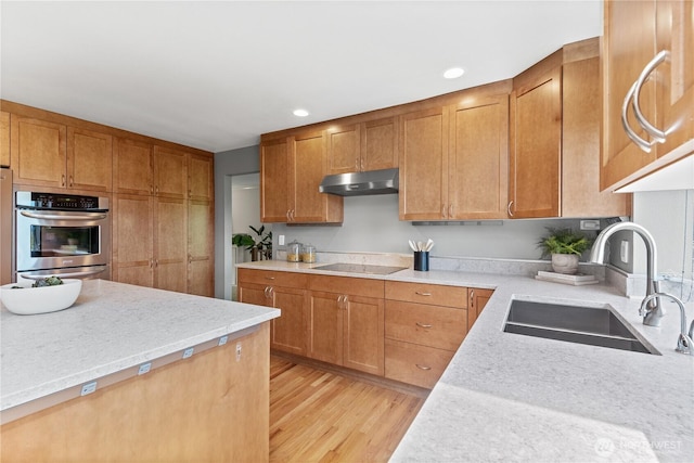 kitchen with a sink, under cabinet range hood, black electric stovetop, light wood-style flooring, and brown cabinetry