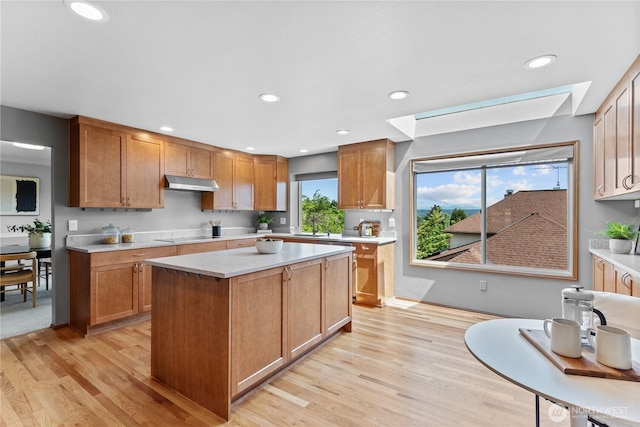 kitchen featuring under cabinet range hood, light countertops, light wood-type flooring, a skylight, and recessed lighting