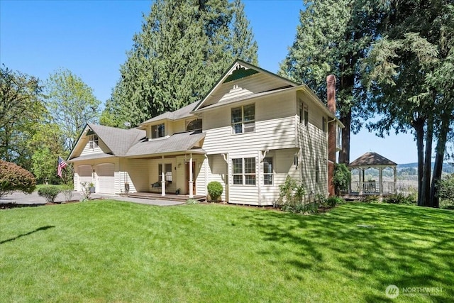rear view of house with a lawn, a gazebo, a chimney, and a garage