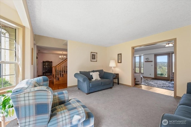 carpeted living room with baseboards, stairs, a textured ceiling, and a chandelier