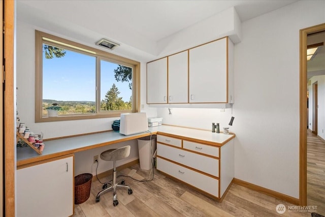 office space featuring baseboards, light wood-style flooring, built in desk, and a wealth of natural light