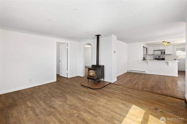 unfurnished living room featuring baseboards, wood finished floors, a wood stove, and a baseboard radiator