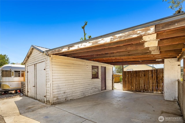 view of outdoor structure featuring fence, a carport, and an outdoor structure
