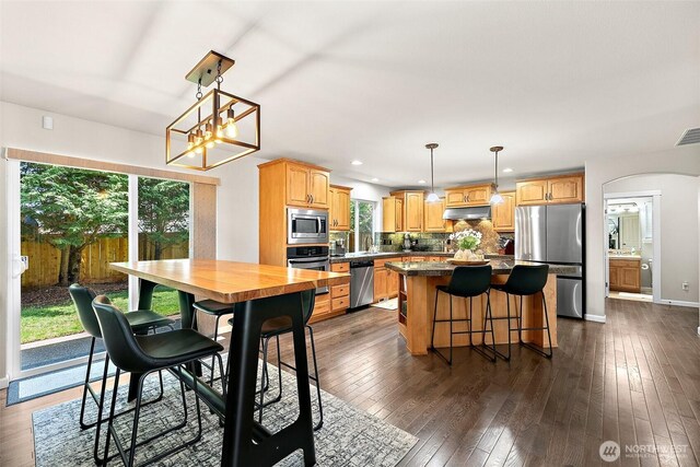 13211 174th St E, Puyallup, WA 98374 - kitchen with stainless steel appliances, under cabinet range hood, a center island, arched walkways, and decorative backsplash