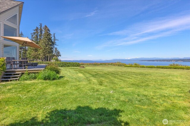 view of green lawn with a deck with water view