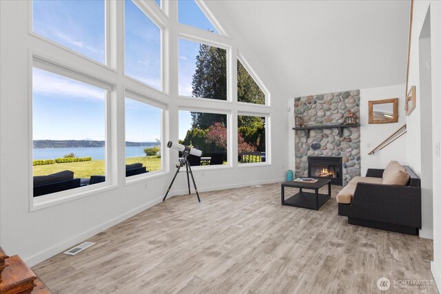 living area with high vaulted ceiling, plenty of natural light, a water view, wood finished floors, and a stone fireplace