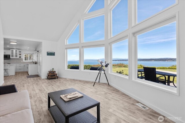 living room featuring high vaulted ceiling, plenty of natural light, a water view, and baseboards