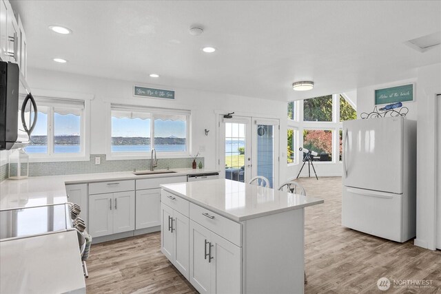 kitchen featuring freestanding refrigerator, a sink, stainless steel microwave, light wood-style flooring, and recessed lighting