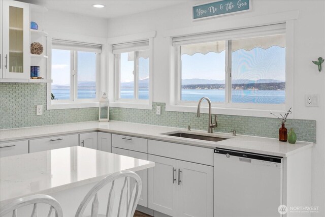 kitchen with dishwasher, a sink, white cabinetry, backsplash, and glass insert cabinets