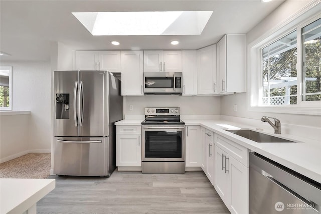 kitchen with recessed lighting, white cabinets, a sink, appliances with stainless steel finishes, and a skylight