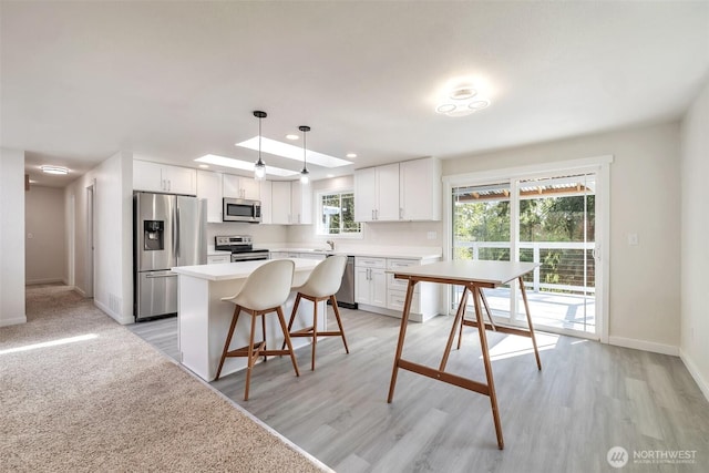 kitchen featuring white cabinets, appliances with stainless steel finishes, a sink, baseboards, and a kitchen island