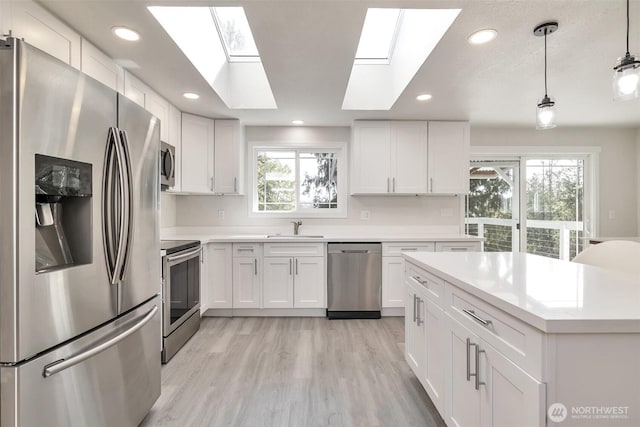 kitchen with a skylight, light countertops, a sink, white cabinets, and stainless steel appliances
