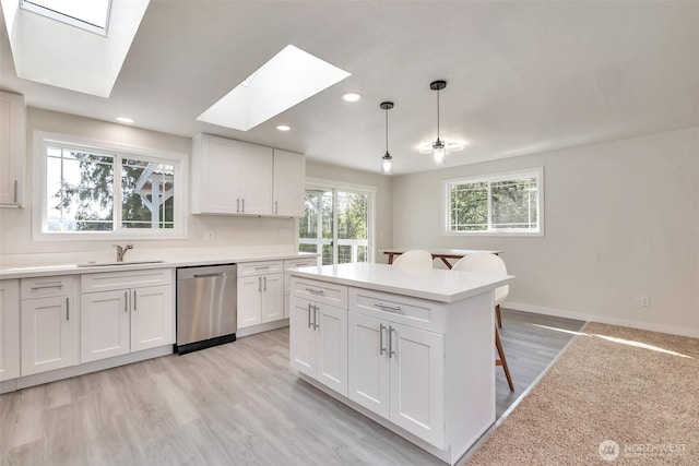kitchen featuring a breakfast bar, white cabinetry, a sink, dishwasher, and a skylight