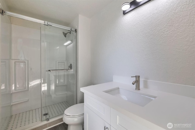 bathroom featuring toilet, a textured ceiling, a shower stall, and vanity