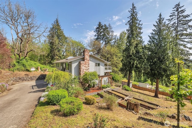 view of home's exterior with a chimney, fence, a vegetable garden, and driveway