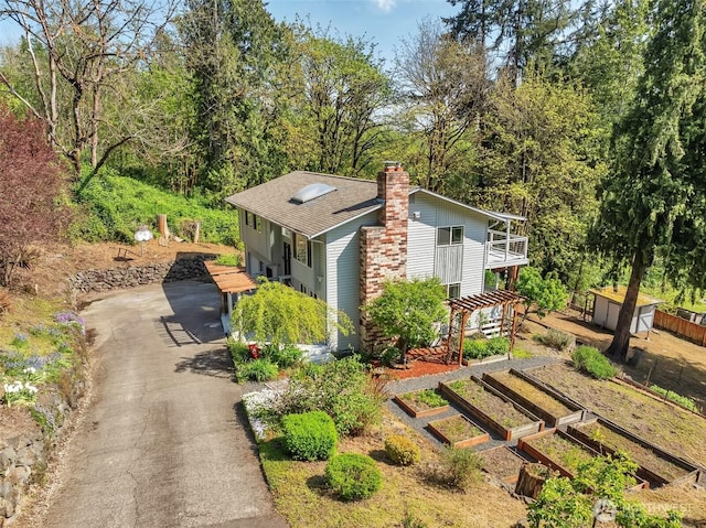 view of side of property with a shingled roof, a chimney, a garden, and driveway