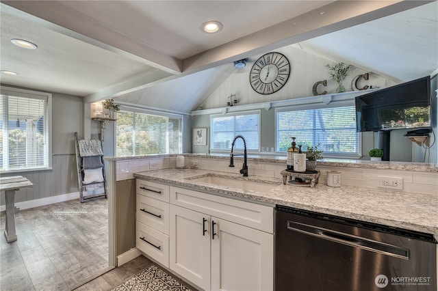 kitchen with stainless steel dishwasher, light wood-style flooring, a sink, a wealth of natural light, and vaulted ceiling with beams