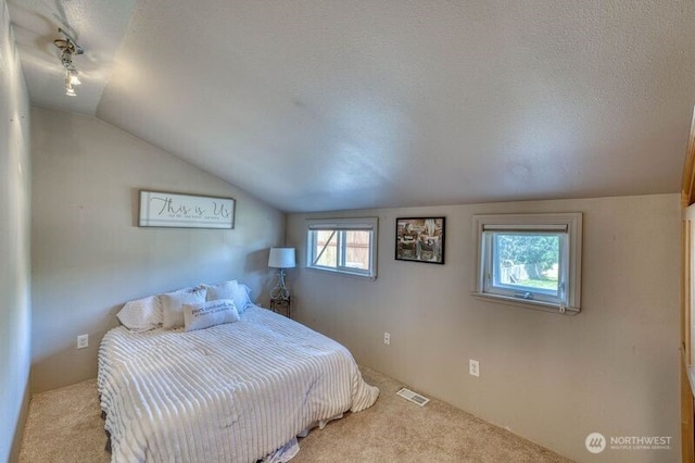 bedroom featuring visible vents, a textured ceiling, lofted ceiling, and carpet