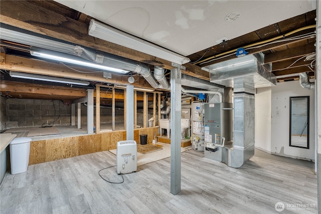 unfinished below grade area featuring water heater, wood finished floors, and heating unit