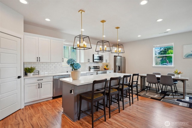 kitchen featuring appliances with stainless steel finishes, a breakfast bar area, light countertops, a center island, and backsplash