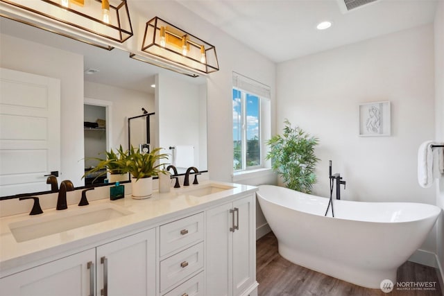 bathroom with double vanity, a sink, wood finished floors, and a soaking tub