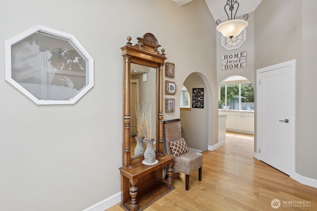 living area with light wood-type flooring, baseboards, arched walkways, and a towering ceiling